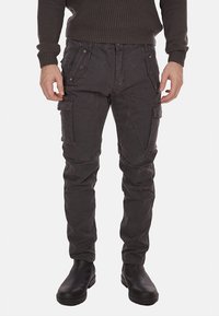 Pantaloni cargo grigi con molteplici tasche, realizzati in un tessuto testurizzato. Presentano una vestibilità slim e gambe affusolate, abbinati a stivali neri.