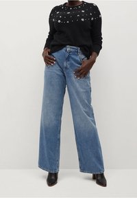 Pull noir avec des embellissements floraux sur le col, associé à un jean en denim bleu clair à jambes larges et des bottines noires à talons.