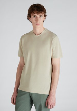 Hellbeige T-Shirt mit kurzen Ärmeln und Rundhalsausschnitt, aus glattem Baumwollstoff. kombiniert mit hellgrünen Hosen, minimalistisches Design.
