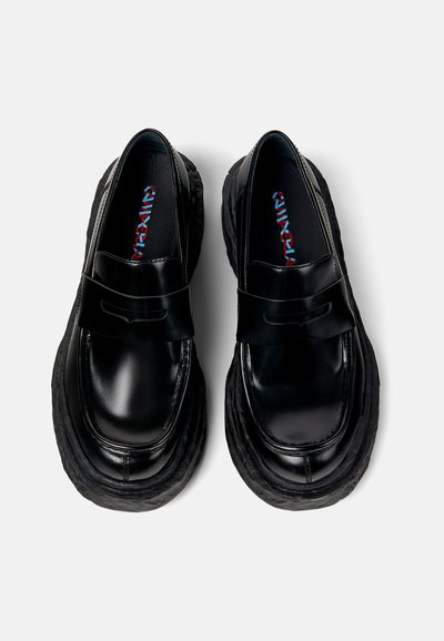 Schwarze Lederloafer mit einer dicken strukturierten Sohle, die mit einer Schleifendetail auf dem Obermaterial und einem kontrastierenden, farbenfrohen Innenmuster versehen sind.