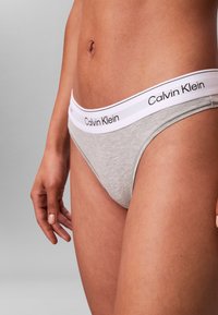 Close-up van een persoon die grijs Calvin Klein ondergoed draagt met een witte tailleband waarop de merknaam in zwarte tekst staat.