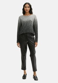 Langärmliger, verlaufender Pullover, der von Hellgrau zu Dunkelgrau übergeht, kombiniert mit glänzenden, schwarzen taillierten Hosen und schwarzen Slipschuhen.