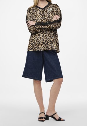 Leopardikuvioinen pitkähihaisen paita V-kaula-aukkolla, yhdistettynä tummansinisistä farkuista valmistettuihin leveälahkeisiin shortseihin ja mustiin korkokenkiin, joissa on siistit hihnat.