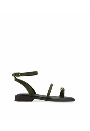 Sandalia plana de ante verde oscuro con tira en el tobillo, dos finas tiras en el pie y detalle de bola dorada en la lazada del dedo.