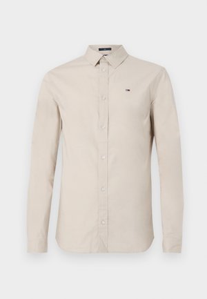 Beige long-sleeve button-up shirt in cotton fabric, featuring a collared neck and small logo embroidery on the left chest. Transparent buttons.