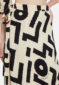 Falda envuelta en negro y crema con patrones gráficos abstractos y audaces. Tela ligera con una textura suave y detalle de lazo lateral.