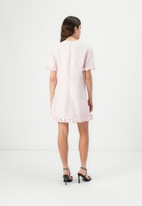 Vestido rosa de mangas curtas com acabamento em babados na barra e nas mangas, apresentando um design reto nas costas e um tecido texturado. Sandálias pretas de salto com detalhes.