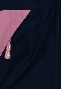 Marineblauer Stoff mit pinkem dreieckigem Akzent und einem Reißverschluss-Zipper mit der Beschriftung "TROLLKIDS". Verfügt über eine glatte Textur und verstärkte Nähte.