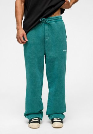 Azurblue joggingbroek met een trekkoord in de taille, met een rechte pasvorm en zijzakken. Gecombineerd met zwarte sneakers en crèmekleurige zolen.