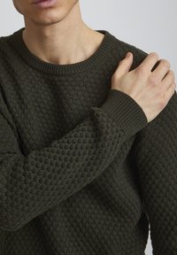 Ciemnozielony sweter o teksturowanym wykończeniu, z prążkowanym okrągłym dekoltem i mankietami, z wzorem w romby na korpusie i rękawach.