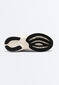 Semelle d'une chaussure de sport beige clair avec des motifs de semelle en caoutchouc noir et le nom de la marque "OYSHO" embossé près de la zone du talon.