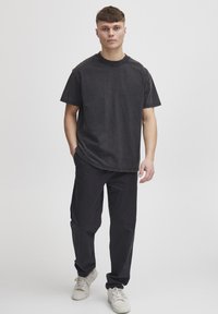 Tricou negru din bumbac cu mâneci scurte și decolteu rotund, asociat cu pantaloni negri din bumbac și adidași albi, având un croi lejer.