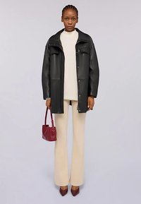 Cappotto in pelle nera con bottoni a pressione, top beige, pantaloni svasati crema e borsa bordeaux. Tessuto liscio, design a strati, dettagli hardware minimalisti.