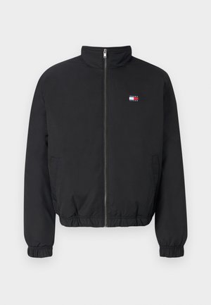 Must värvi bomber-jakk kõrge krae, esikinnitus, elastsete mansettide ja alumise äärega. Omab väikest logo punase, valge ja sinise värviga.