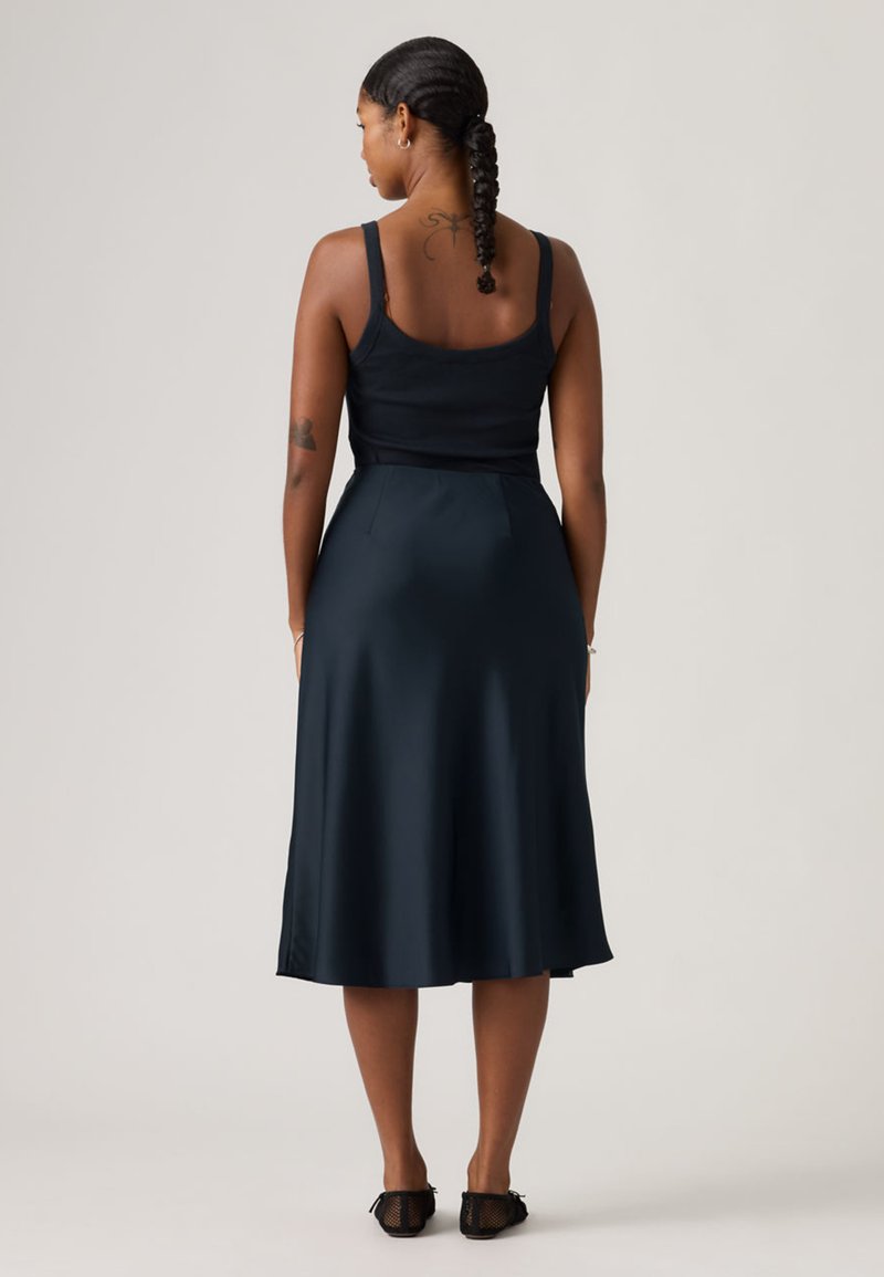 Navy satin dress with a fitted bodice and flared skirt. Features thin straps and a smooth texture, reaching mid-calf. Black footwear.