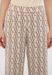 Pantalon de détente à motifs présentant un design géométrique beige et crème. Fabriqué en tissu doux avec une ceinture élastique, garantissant un confort optimal.