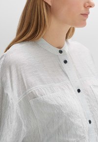 Lightweight, striped shirt in white and navy blue, featuring a round collar, three buttons, and a front pocket with a smooth texture.