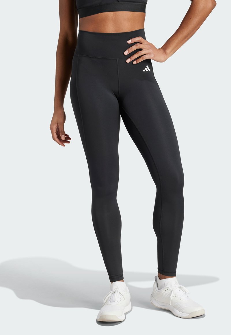 Svarta högmidjade leggings med en slät textur och åtsittande design, med en vit logotyp och sömdetaljer längs sömmarna.