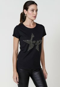 Zwarte katoenen t-shirt met een sterontwerp van rhinestones. Korte mouwen en een ronde halslijn. Gemaakt in combinatie met zwarte gestructureerde broek.