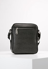Black crossbody bag featuring a textured surface with an embossed Valentino logo, a zippered front pocket, and an adjustable strap.