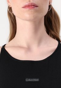 Top nero senza maniche con scollatura rotonda, realizzato in tessuto a coste. Presenta un'etichetta grigia Calvin Klein cucita sul davanti.