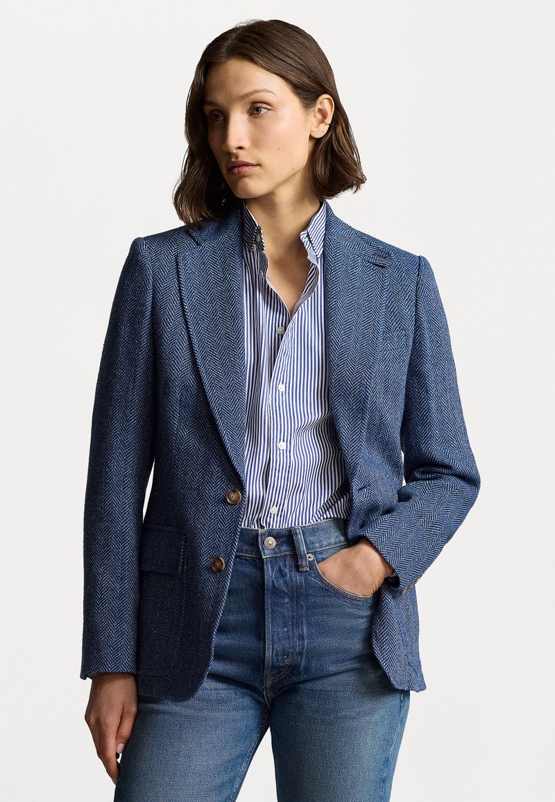 Svetlo modra herringbone blazer z ipkasto rešetkastim vzorcem, z nazobčanimi klapami, dvema gumboma in sprednjimi žepi, v kombinaciji z modro in belo prugastim srajcem ter kavbojkami.