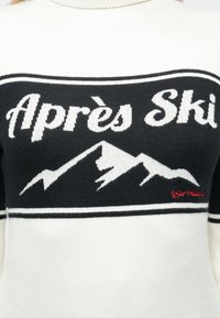 Hvitt og svart genser med hvit tekst «Après Ski» over en hvit fjellgrafikk med små røde detaljtekster på høyre side.