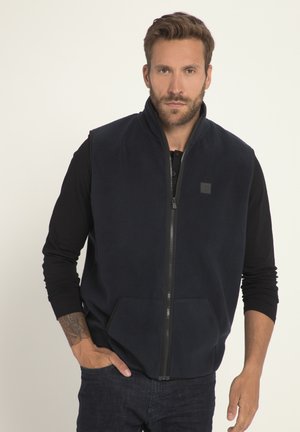 Chaleco de forro polar azul marino con cuello alto, cierre completo y dos bolsillos frontales. Presenta un parche de logo cuadrado en el lado izquierdo del pecho y una superficie texturizada.