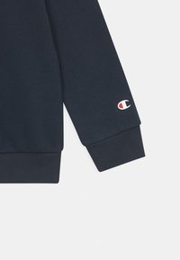 Manga de sudadera navy hecha de tela texturizada, con un puño acanalado y un pequeño logo en blanco, rojo y azul en la muñeca.