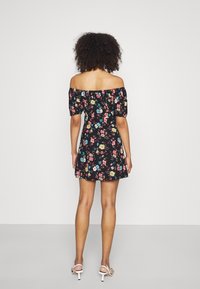 Czarna, kwiecista sukienka z odkrytymi ramionami i bufkami na rękawach, zdobiona kolorowymi kwiatami. Sukienka ma dopasowaną talię i rozkloszowany dół. Noszona z białymi szpilkami.