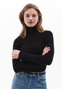 Schwarzer gerippter Rollkragenpullover mit langen Ärmeln, kombiniert mit hochtaillierten blauen Jeans und einem schwarzen Gürtel. Einfaches, figurbetontes Design.