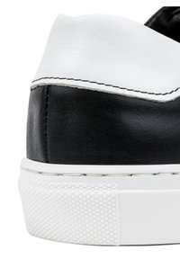 Czarno-białe trampki z gładką skórzaną cholewką, z białą gumową podeszwą o teksturowanym wzorze oraz ozdobnym przeszyciem wzdłuż krawędzi.