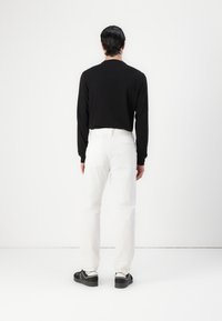 Zwarte langgesleeve shirt, witte recht gesneden broek en zwarte sneakers. Eenvoudig ontwerp zonder zichtbare patronen of logo's. Strakke lijnen en neutrale kleuren.