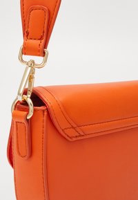 Borsa a spalla in pelle arancione con un design elegante, hardware dorato e bordi cuciti. Include una tracolla rimovibile per una maggiore versatilità.