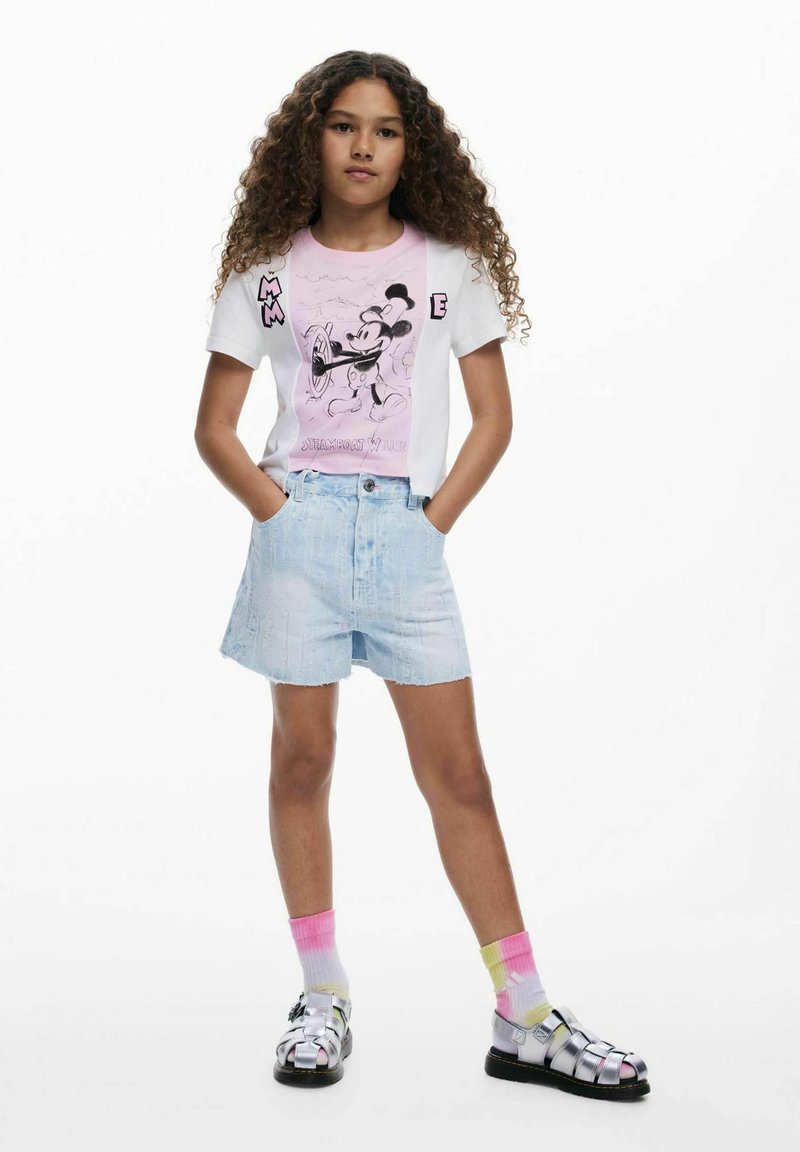 Hvid t-shirt med et pink Mickey Mouse grafik, lyse denim shorts og farverige knæhøje strømper med sandaler, der har en skinnende, metallisk finish.