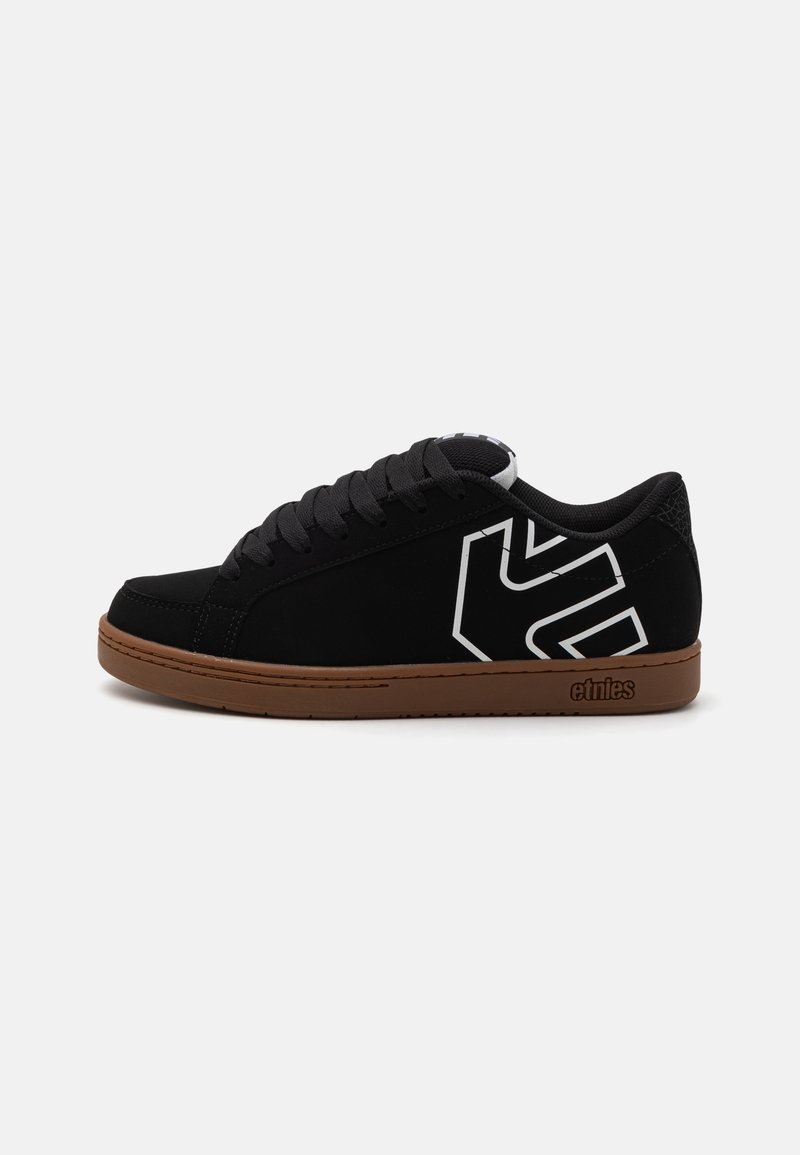 Schwarze Sneaker mit sueded Textur, featuring ein weißes Logo an der Seite und einer braunen Gummisohle. Schnürverschluss und flaches Design.