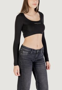 Czarny krótki top z długim rękawem o okrągłym dekolcie i małym białym logo. W połączeniu z ciemnoszarymi dżinsami o klasycznym, pięciokieszeniowym kroju.