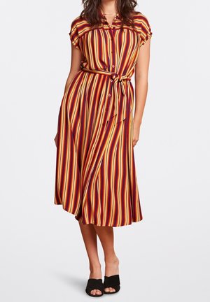 Femme portant une robe midi à boutons, rayures verticales multicolores, manches courtes, ceinture nouée à la taille, et chaussures noires ouvertes à enfiler.