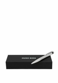 Penna a sfera in metallo argentato con impugnatura testurizzata e dettagli in cromo, posizionata su una scatola nera contrassegnata con "HUGO BOSS" in lettere bianche.