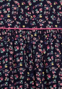 Sukienka z kwiecistym wzorem ma granatowe tło, wielokolorowe kwiaty i różową lamówkę w talii. Plisowany fason dodaje objętości.