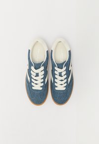 Temne modri denim superge z belimi vezalkami in dodatki. Imajo teksturirano zgornjo tkanino in gumijast podplat. Priložnostna športna zasnova.