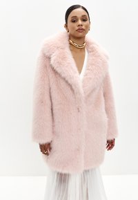 Lyserød faux fur frakke med bred krave, drop skuldre og lange ærmer, der har en blød tekstur og en enkelt knaplukning.