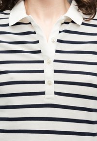 Κοντινό πλάνο ενός ατόμου που φοράει λευκό πόλο πουκάμισο με μαύρες οριζόντιες ρίγες και τρία λευκά κουμπιά στο μανσόν.