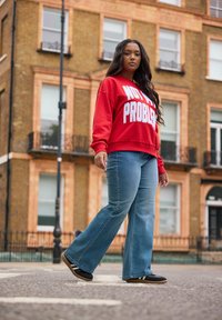 Punainen huppari, jossa lukee "EI OLE MINUN ONGELMA", valkoisilla kirjaimilla, yhdistettynä vaaleansinisiin leveälahkeisiin farkkuihin, joissa on hopeisia niittejä. Käytetään mustien kenkien kanssa.