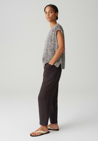 Zwart-wit gestreept topje met korte mouwen; gecombineerd met donkere broek en beige schuifsandalen. Soepele texturen, relaxte pasvorm en casual stijl.