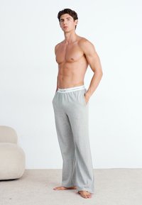 Graue Strick-Loungehosen mit einem elastischen Bund, der ein weißes Markenlabel zeigt. Leichter Stoff, lockere Passform und Seitentaschen.