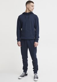 Donkerblauwe hoodie met een voorvak, capuchon met trekkoord en geribde mouwen, gecombineerd met bijpassende joggingbroek en zwarte sneakers.