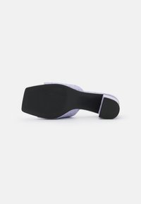 Semelle et talon d’une mule lilas à bout carré, motif texturé et grip en caoutchouc noir au-dessous sur fond blanc.
