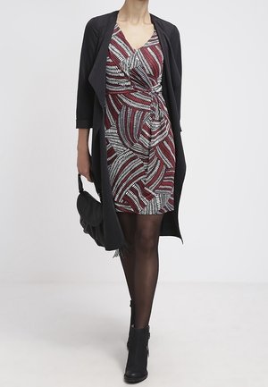 Svart cardigan över en röd- och vitmönstrad klänning med knutdetalj, kombinerad med svarta ankelstövlar och en axelremsväska.