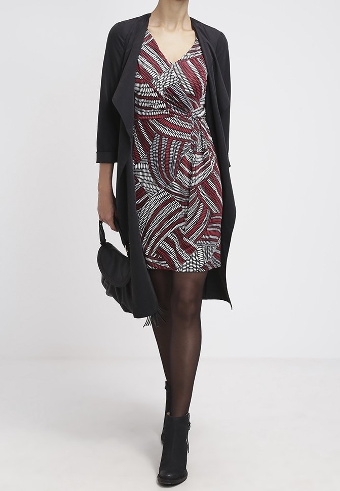 Černý kardigan přes červené a bílé šaty s vzorem a detaily uzlu, doplněné černými kotníkovými botami a kabelkou přes rameno.